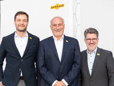 Drie mannen staan voor een aanhangwagen met een wit zeil. | © Humbaur GmbH
