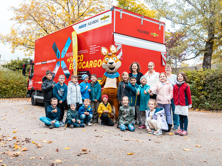 Maskottchen Blicki zusammen mit Kindern vor einem roten LKW | © Humbaur GmbH