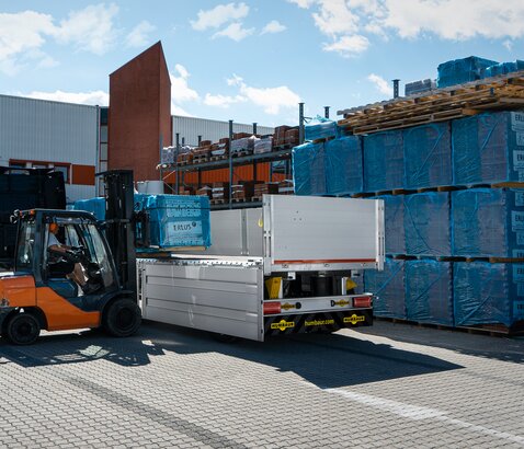 Devant un magasin de bricolage, des matériaux de construction sont chargés dans une remorque à l'aide d'un chariot élévateur. | © Humbaur GmbH