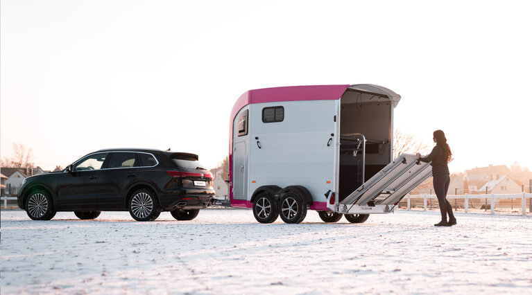 A woman opens the tailgate of the Equitos Alu, which is coupled to a car